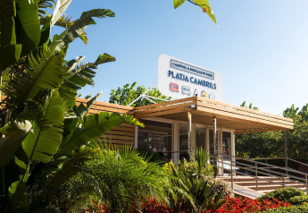 Entrada al Camping & Bungalow Park Platja Cambrils rodeada de plantas tropicales y ambiente soleado.