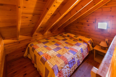 Et hyggeligt soveværelse med træpaneler og skrå loft, dobbeltseng og natbord på La Llosa 1 Xaloc i Spanien.