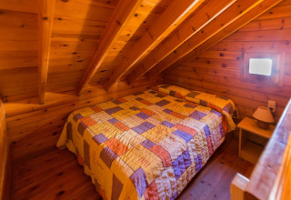 Et hyggeligt soveværelse med træpaneler og skrå loft, dobbeltseng og natbord på La Llosa 1 Xaloc i Spanien.