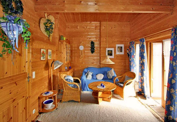 Séjour chaleureux en bois avec canapé bleu, fauteuils en rotin et rideaux fleuris, en Allemagne.