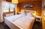 Bedroom in wooden chalet at Holiday Park Lauterdörfle, double bed, window, and wall art in Germany.