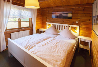 Bedroom in wooden chalet at Holiday Park Lauterdörfle, double bed, window, and wall art in Germany.