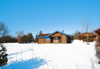 Houten chalets in Holiday park Lauterdörfle op een besneeuwd terrein met blauwe lucht in Duitsland.