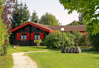 Chalet du parc de vacances Lauterdörfle avec volets rouges, pelouse verte et arbres, en Allemagne ensoleillée.