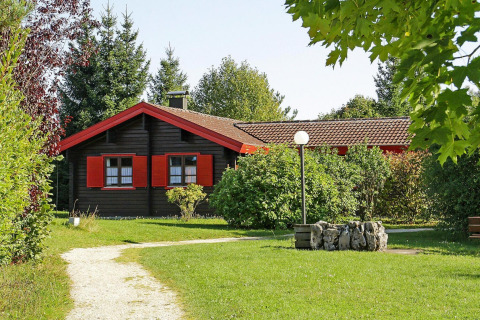 Chalet in vakantiepark Lauterdörfle met rode luiken, groene tuin en bomen, zonnig Duitsland.
