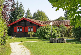 Chalet en el parque vacacional Lauterdörfle con contraventanas rojas, césped verde y árboles en Alemania.