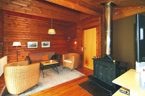 Knusse woonkamer van blokhut met houtkachel, rieten stoelen en houten muren in Lauterdörfle, Duitsland.