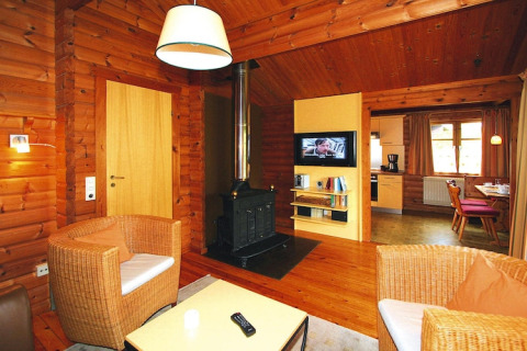 Acogedora sala de chalet con paredes de madera, estufa, sillones de mimbre y vista a la cocina.