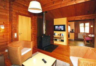 Soggiorno accogliente in chalet con pareti in legno, stufa, poltrone in vimini e vista cucina.