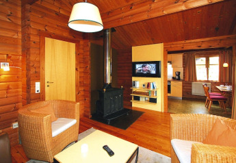 Cozy chalet living room with wooden walls, stove, wicker chairs, and a view into the kitchen area.