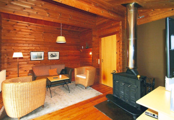 Cozy chalet living room with wood-paneled walls, fireplace, wicker chairs, and a soft rug.