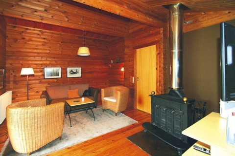 Soggiorno accogliente in chalet con pareti in legno, stufa, poltrone in vimini e tappeto morbido.
