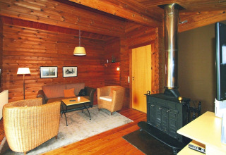 Salon douillet de chalet avec murs en bois, poêle à bois, fauteuils en osier et tapis moelleux.