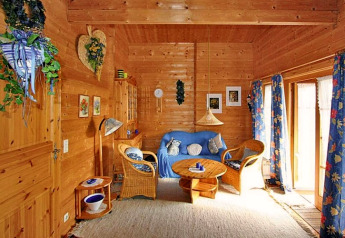 Cozy chalet living room with wooden walls, wicker chairs, blue sofa, and floral blue curtains in sunlight.
