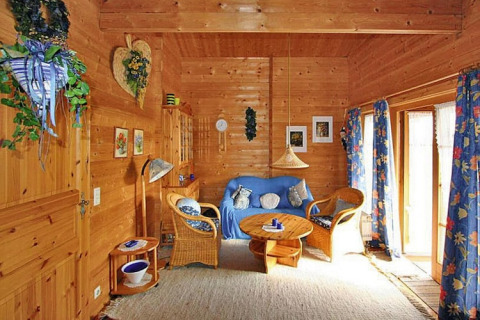 Accogliente soggiorno in chalet con pareti in legno, sedie in vimini, divano blu e tende floreali blu.