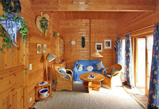 Acogedora sala de estar en un chalet de madera, con sillas de mimbre, sofá azul y cortinas florales azules.