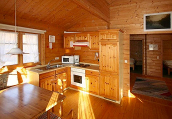 Cozy wood-paneled kitchen and dining area inside a chalet, warmly lit by natural sunlight from windows.
