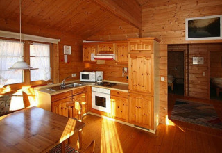 Cuisine et coin repas en bois chaleureusement éclairés dans un chalet, baignant dans la lumière naturelle.
