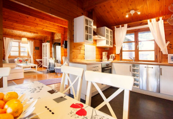 Bright chalet kitchen and living area with wood paneling, large windows, and modern white furniture.
