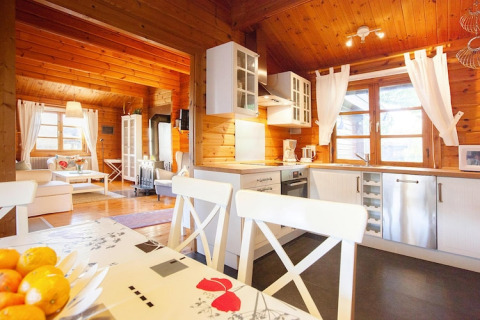 Cucina e soggiorno di uno chalet luminoso, con pannelli in legno, grandi finestre e arredi moderni.