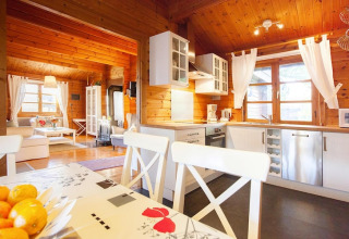 Bright chalet kitchen and living area with wood paneling, large windows, and modern white furniture.