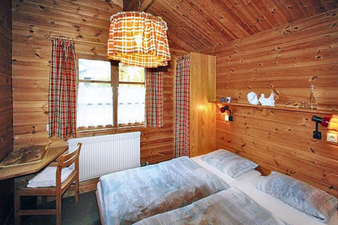 Chambre chaleureuse dans un chalet en bois, avec rideaux à carreaux, deux lits et lumière tamisée.