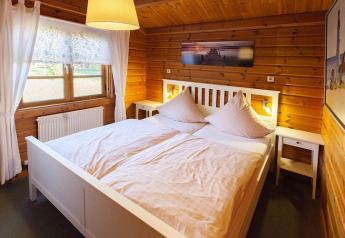 Acogedor dormitorio de chalet de madera con cama doble blanca, cortinas claras y luz cálida ambiente.