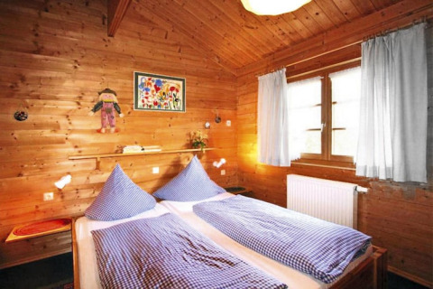 Accogliente camera da letto in chalet di legno con due letti singoli, biancheria a quadretti e tende chiare.