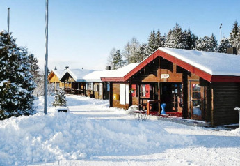 Met sneeuw bedekte houten chalets in een rustige winterse omgeving, omringd door dennenbomen en blauwe lucht.