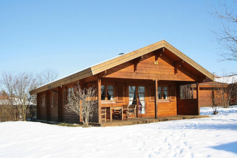 Chalet in legno con veranda e mobili da esterno, circondato da neve e alberi spogli in una giornata d’inverno.