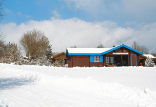 Chalet in legno con rifiniture blu immerso nella neve, circondato da alberi sotto un cielo nuvoloso.