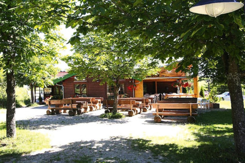 Panchine e tavoli di legno sotto alberi verdi davanti a uno chalet accogliente in una giornata soleggiata.