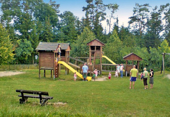 Photo of a playground at a chalet, showing children playing and adults standing around wooden structures.