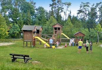 Foto de un área de juegos en un chalet, con niños jugando y adultos observando cerca de estructuras de madera.