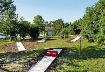 Outdoor mini-golf course at a chalet surrounded by greenery on a bright, sunny summer day.