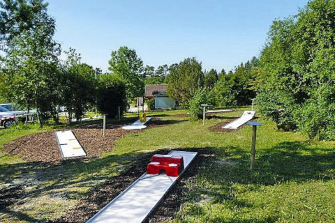 Campo de minigolf al aire libre junto a un chalet rodeado de naturaleza bajo el sol de verano.