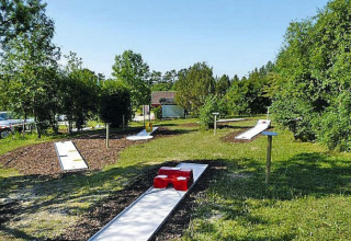 Parcours de mini-golf en plein air près d’un chalet entouré de verdure par une journée ensoleillée.