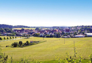 View from a chalet overlooking green fields and a charming village with red roofs under a clear sky.