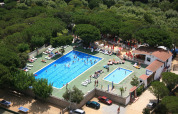 Aerial view of a glamping site featuring two swimming pools, sun loungers, and forest surroundings.