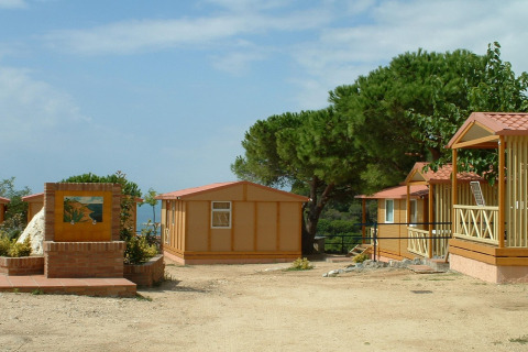 Bungalows og grønne træer på Camping Rocagrossa til 4 personer i Spanien, set under en blå himmel.