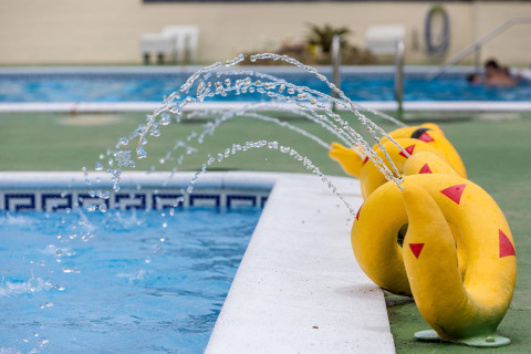 Gelbe wasserfontänenförmige Figuren sprühen Wasser am Beckenrand eines Pools in einer Lodge.