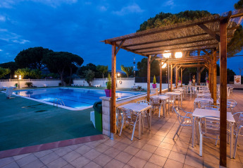 Espace repas extérieur avec vue sur piscine dans un hébergement glamping, entouré d’arbres et de lumières.