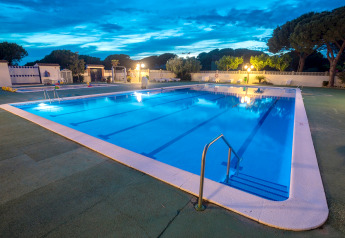Piscine éclairée au crépuscule dans un hébergement glamping, entourée d’arbres et de lumières extérieures.