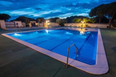 Beleuchteter Swimmingpool bei Dämmerung in einer Glamping-Unterkunft mit Bäumen im Hintergrund.