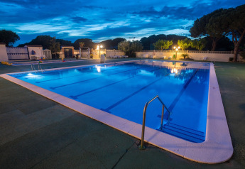 Illuminated swimming pool at dusk in a glamping accommodation, surrounded by trees and outdoor lights.