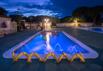 Piscine éclairée avec décorations ludiques et jets d'eau dans un hébergement glamping le soir.