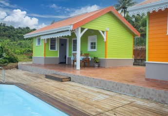 Colorful cabin bungalow with terrace and pool in lush countryside, set against a blue sky background.