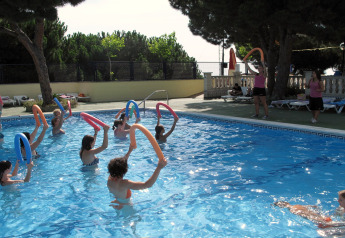 Personen doen watergym met schuimrubberen buizen in een openluchtzwembad bij een glamping accommodatie.