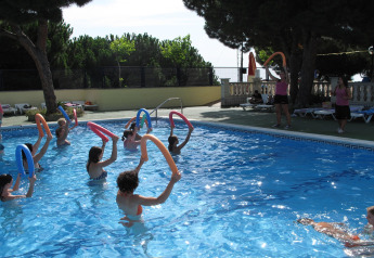 People enjoy water aerobics with pool noodles in an outdoor pool at a glamping accommodation in summer.