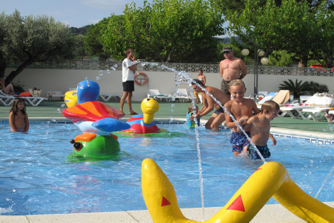 Kinder spielen in einem seichten Swimmingpool mit buntem Wasserspielzeug in einer Lodge.